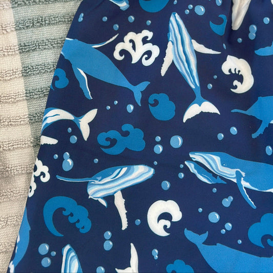 Navy swim shorts with whale pattern on a textured surface with goggles.