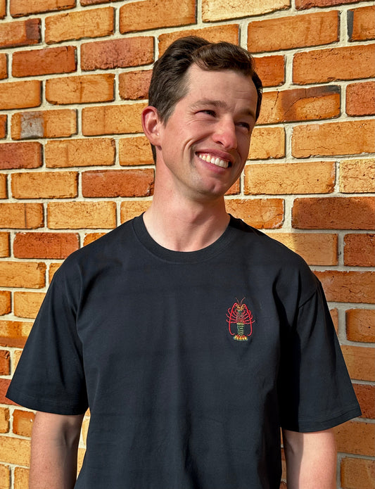 Man wearing a navy t-shirt with a lobster logo against a brick wall