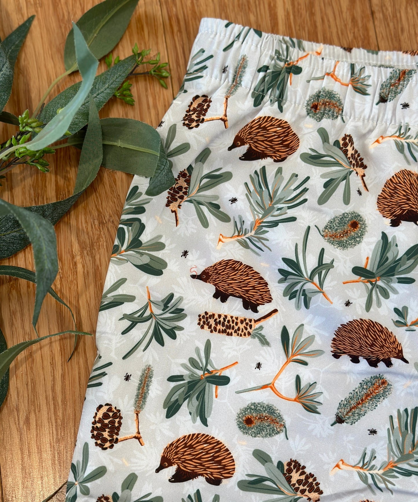 Shorts with echidna and banksia pattern on a wooden surface