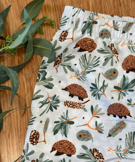 Shorts with echidna and banksia pattern on a wooden surface