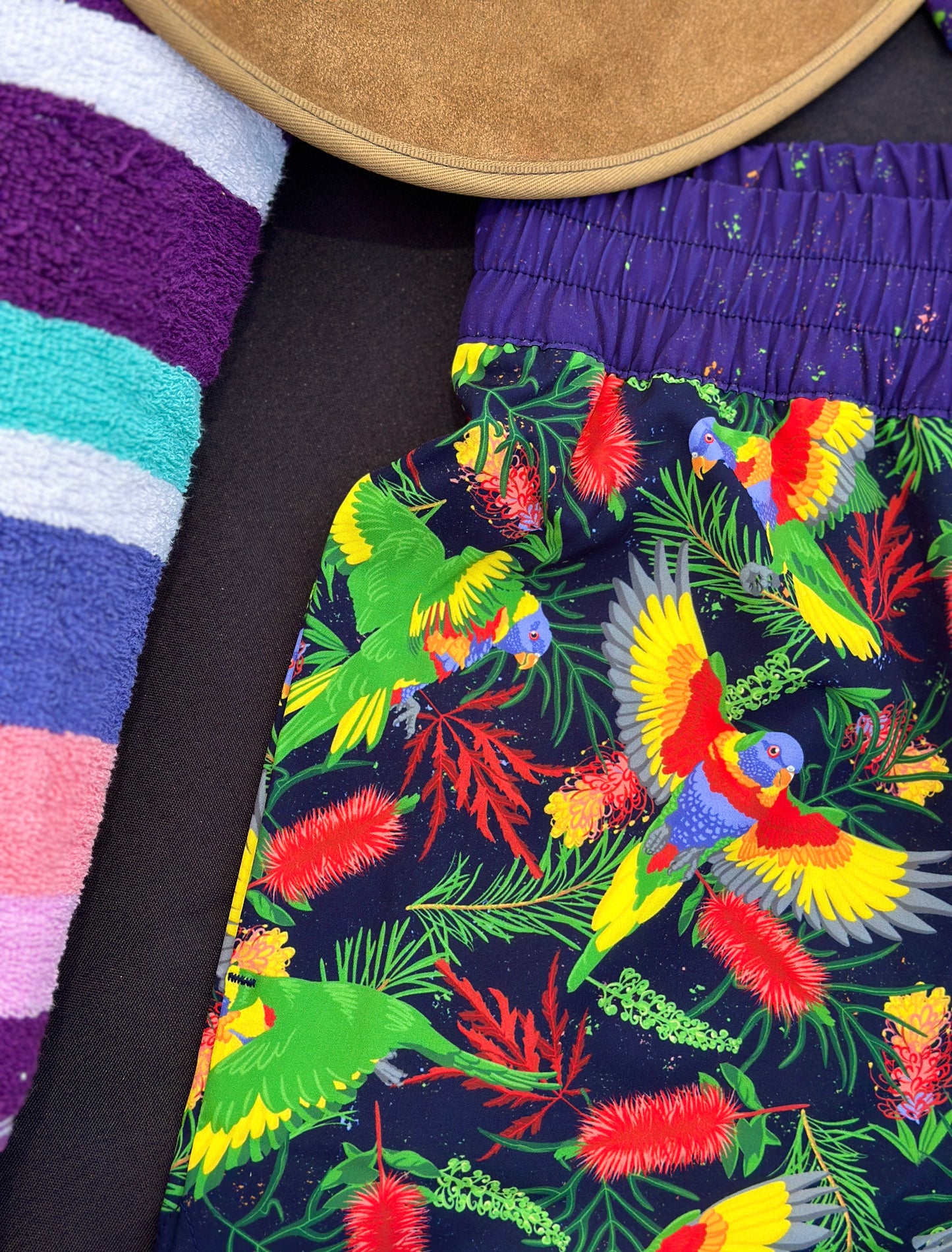 Colorful rainbow lorikeet-patterned shorts with a striped towel in the background