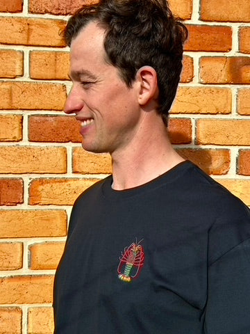 Man wearing a navy t-shirt with a lobster logo against a brick wall.