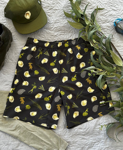 Dark Navy shorts with green seaweeds, and oysters pattern on a white textured surface with a green cap and plant.