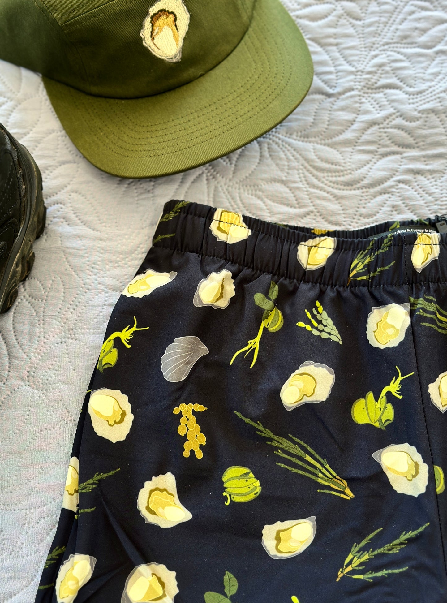 Dark Navy shorts with green seaweeds, and oysters pattern on a white textured surface with a green oyster cap.