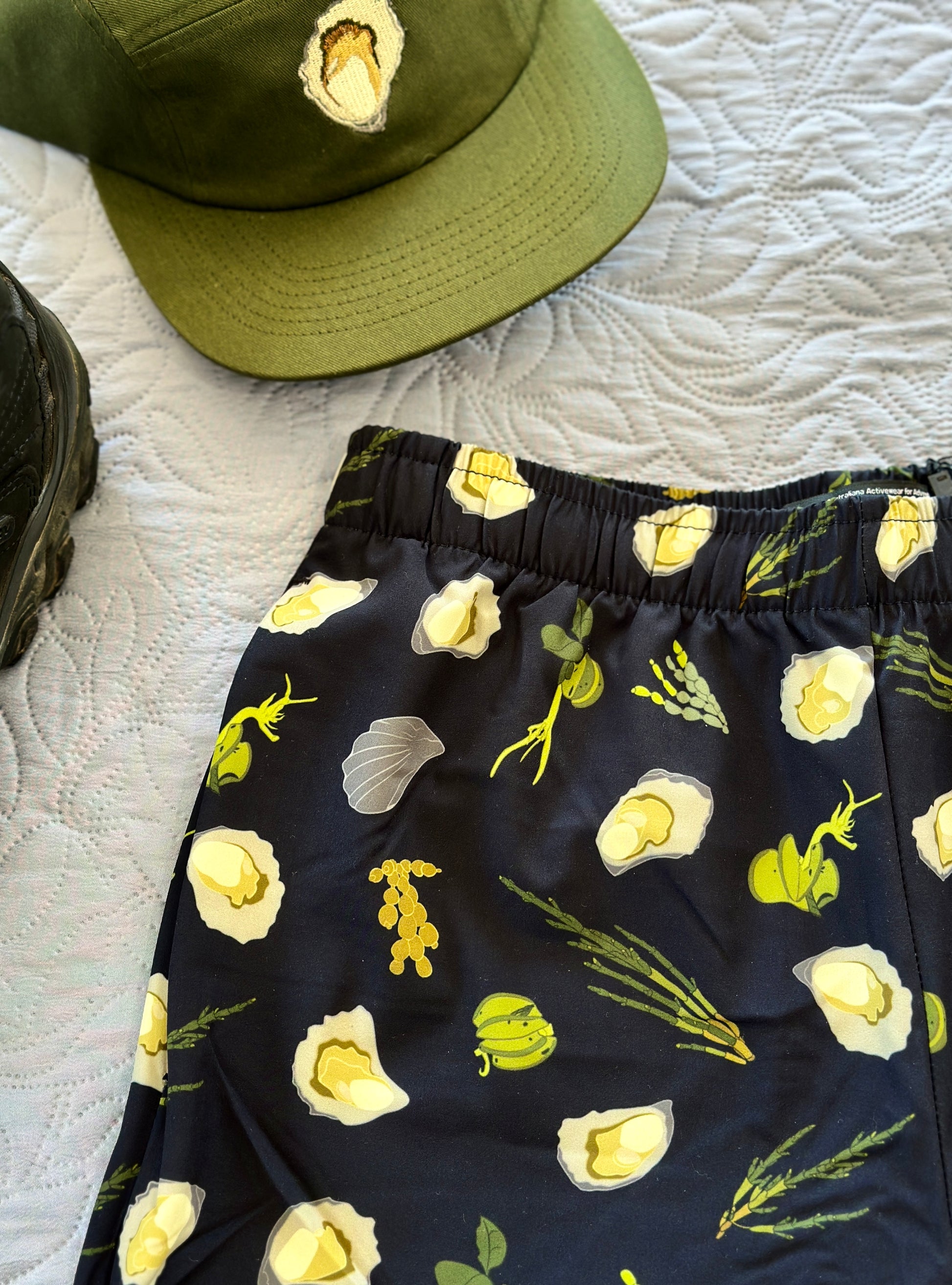 Dark Navy shorts with green seaweeds, and oysters pattern on a white textured surface with a green oyster cap.