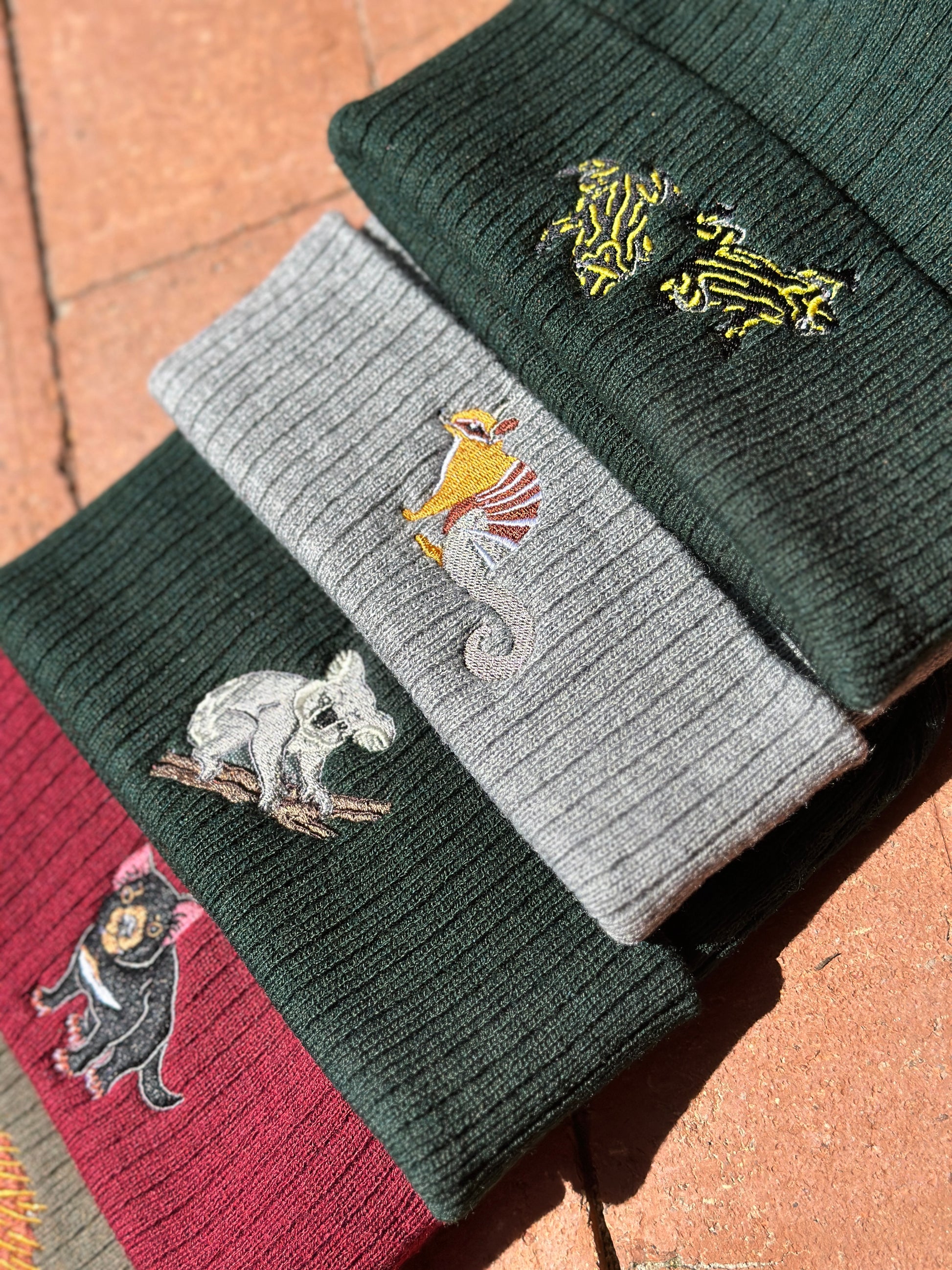 Stack of beanies with embroidered animal designs on a textured surface