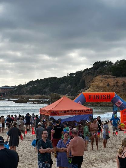 Beach event with people, tents, and a 'Finish' archway under a cloudy sky.