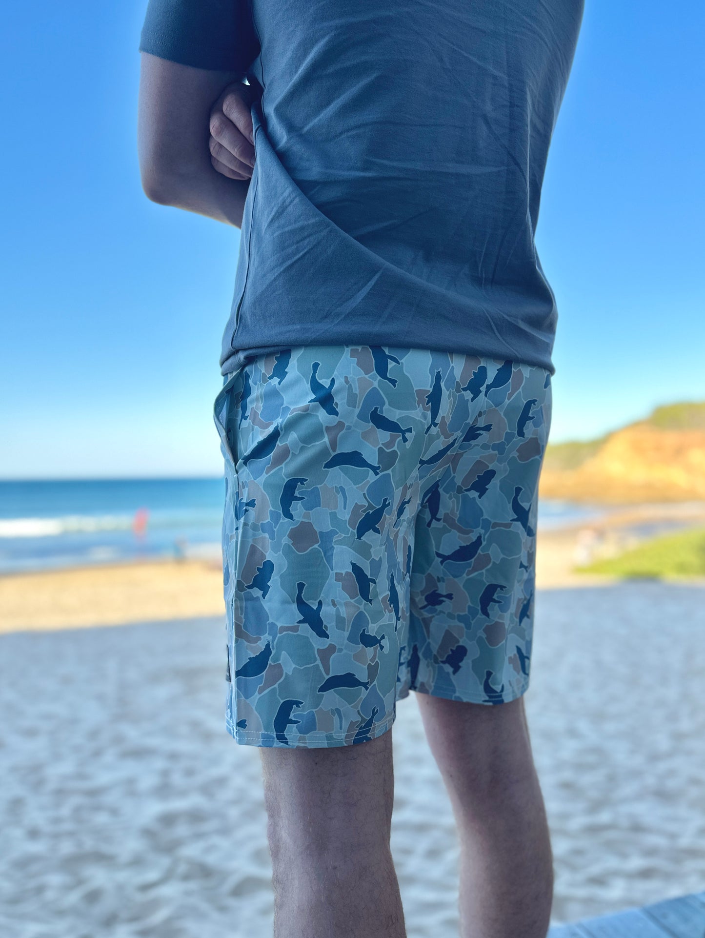 Person wearing blue shorts with a seal pattern at a beach.