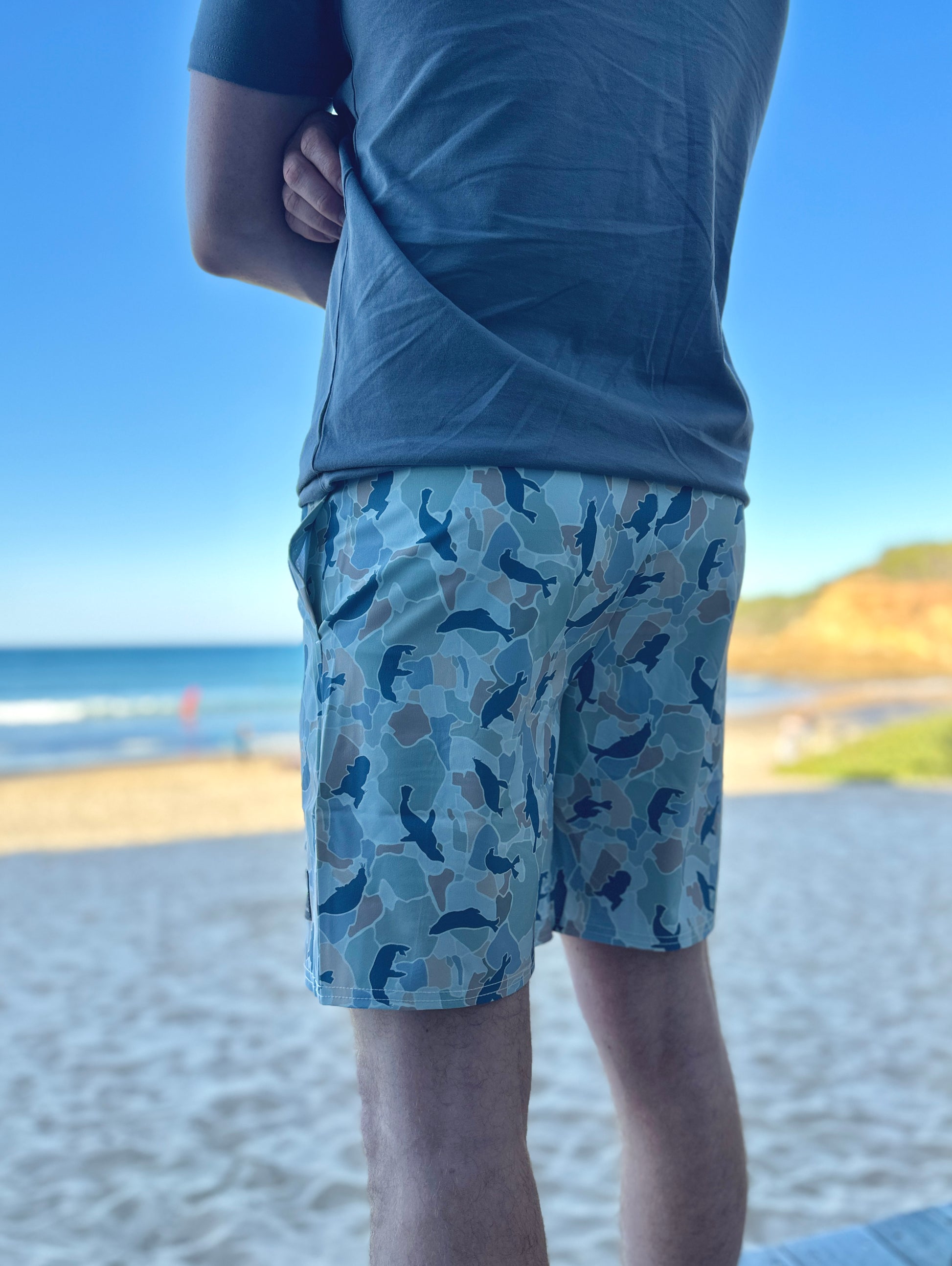 Person wearing blue shorts with a seal pattern at a beach.